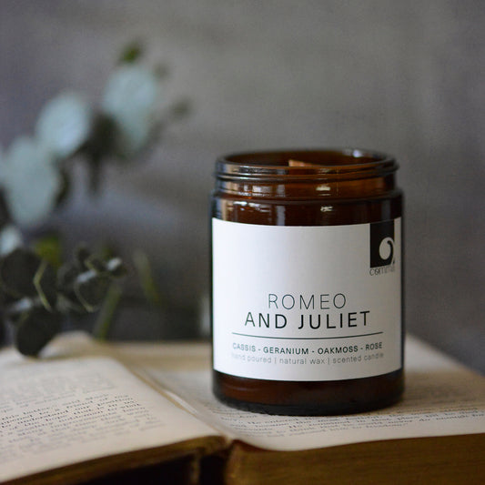 Romeo and Juliet amber jar candle sitting on top of an open antique book and blurred dark background